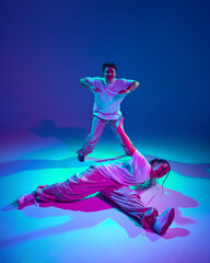 Talented young man and woman in casual sports clothes dancing hip-hop against purple studio background in neon light. Dance show. Concept of contemporary dance, hobby, youth