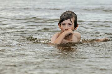 A young child struggling and shouting in the water, appearing to be in distress, with splashes around him and a vast expanse of water in the background. The scene evokes a sense of urgency and concern