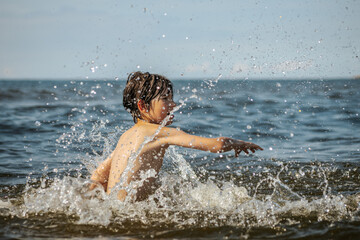 Fototapeta premium A young child struggling and shouting in the water, appearing to be in distress, with splashes around him and a vast expanse of water in the background. The scene evokes a sense of urgency and concern