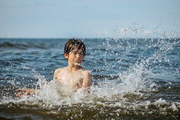 Fototapeta premium A young child struggling and shouting in the water, appearing to be in distress, with splashes around him and a vast expanse of water in the background. The scene evokes a sense of urgency and concern