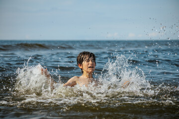 A young child struggling and shouting in the water, appearing to be in distress, with splashes around him and a vast expanse of water in the background. The scene evokes a sense of urgency and concern