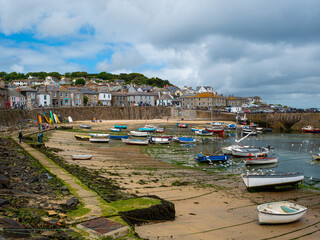 Fishing and sailing boats moored at low tide in harbour at Mousehole, a fishing port in Penzance on the shore of Mount's Bay in Cornwall, England. Cloudy sky. Text space.