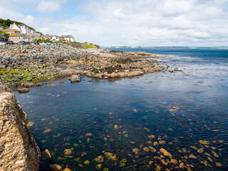The rocky shoreline at Marazion in Mount's Bay, Penzance, Cornwall, UK, with bright blue sea, hillside houses, cloudy sky.  