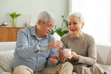 Saving money investment for future. Senior adult mature couple holding piggy bank putting money...