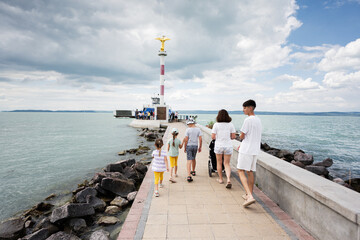Family walking towards a lighthouse on a pier in Siofok, Balaton lake, Hungary under a cloudy sky