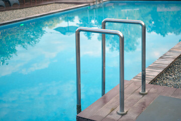 Metal pool ladder leading into a clear blue swimming pool with wooden decking and gravel surround