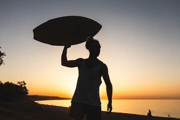 unrecognizable A man is holding a surfboard while standing on a beach at sunset