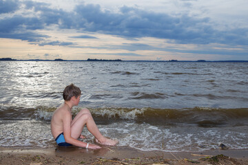 A boy sits on the seashore.