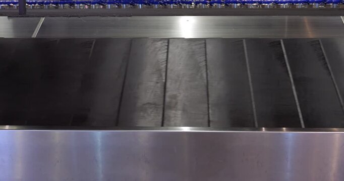 Close view of empty slat conveyor in baggage claim hall of airport. Black slats of typical luggage belt move quickly under dim lighting. No bags and no people are visible in this shot