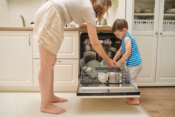 Parent and child loading dishwasher together in a kitchen. Indoor lifestyle photography. Home chores and family responsibility concept. Kid aged three years (three year old boy)