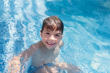 A cute little boy is standing in the children's outdoor pool, smiling. Childhood. Summer. Holidays