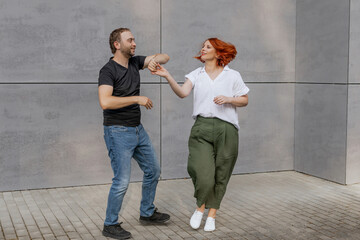 Happy dancers curling in dance in city. Romantic couple, woman with red hair and man in dark...