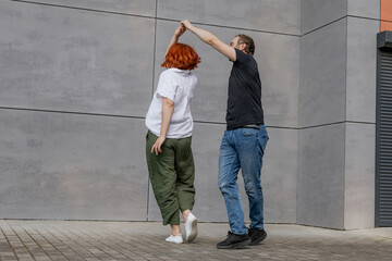 Happy dancers curling in dance in city. Romantic couple, woman with red hair and man in dark...
