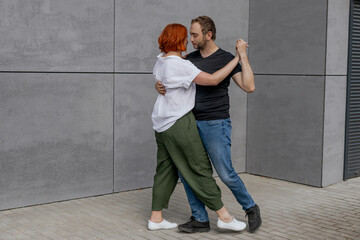 Happy dancers curling in dance in city. Romantic couple, woman with red hair and man in dark...