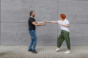 Happy dancers curling in dance in city. Romantic couple, woman with red hair and man in dark...