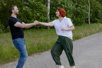 Happy dancers curling in dance in park. Romantic couple, woman with red hair and man in dark...