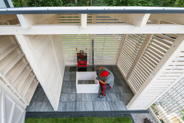 Person Assembling Wooden Structure in Modern Outdoor Space Surrounded by Trees