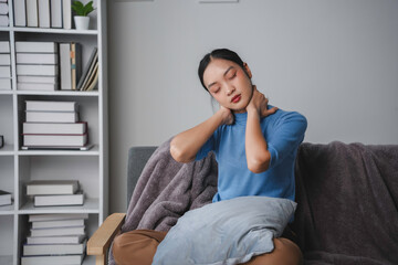 Young woman is massaging her neck, suffering from neck pain while sitting on a sofa at home