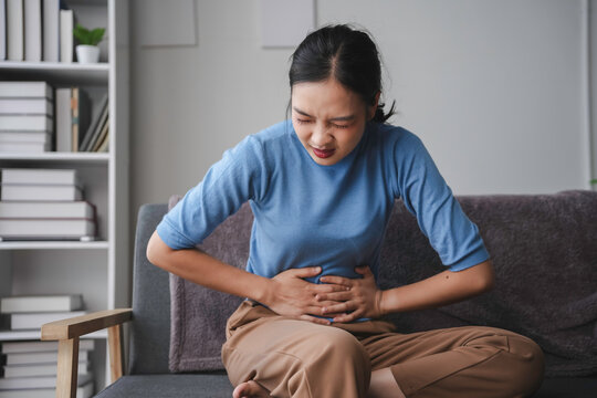 Young woman is experiencing intense abdominal pain, clutching her stomach in discomfort while at home