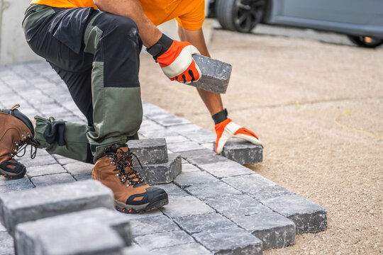 Worker Laying Paving Stones on a Driveway at a Construction Site in Bright Daylight
