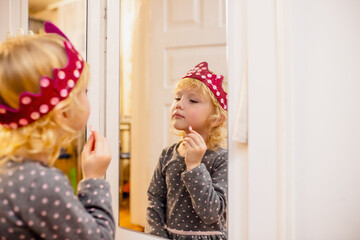 Young Girl Applying Lipstick While Gazing at Reflection in Mirror Inside Playroom