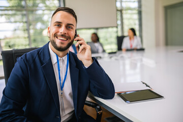 Portrait of businessman sitting in his office in the middle of the meeting talking on the phone.