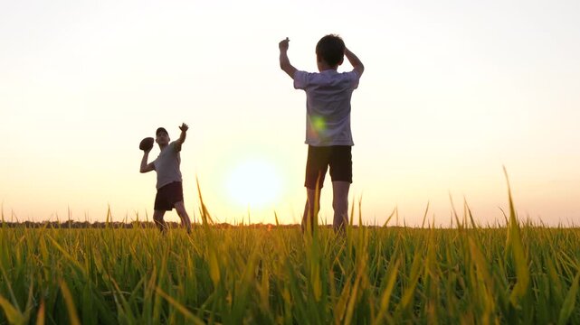 happy dad playing rugby with his son. dad throws a rugby ball to his son. family playing American football at golden hour in the park.