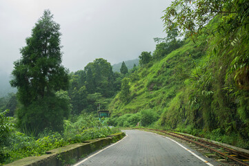 Concrete road passing through Himalayan mountains and lush green forest. Scenic natural beauty of monsoon in Darjeeling, West Bengal, India.