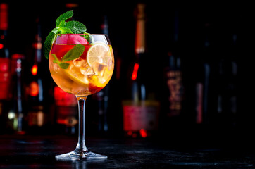 Summer sangria cocktail with pink wine, peach, orange and ice. Black background with  bottles