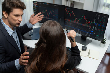 Two business traders discussing on dynamic stock market in currency rate investment trading on two pc screens with compare real time graph on risk or profit point of data at modern office. Postulate.