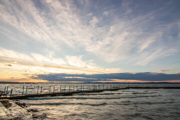 Water landscape taken from the shore of a calm lake. View over the reflecting water to the horizon in the sunset. a jetty or pier at Siofok harbor, Balaton, Hungary
