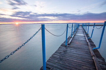 Water landscape taken from the shore of a calm lake. View over the reflecting water to the horizon in the sunset. a jetty or pier at Siofok harbor, Balaton, Hungary