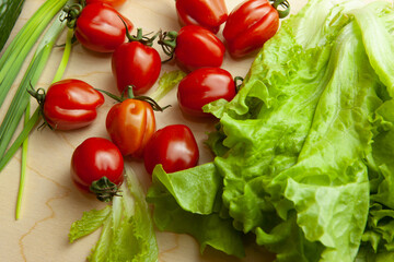 Fresh lettuce leaves and tomatoes on wood table, top view. Salad background from fresh vegetable for poster, calendar, post, screensaver, wallpaper, postcard, cover, website. High quality photo