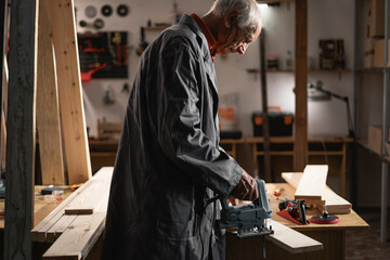 Elderly Carpenter Cutting Wooden Board with Jigsaw