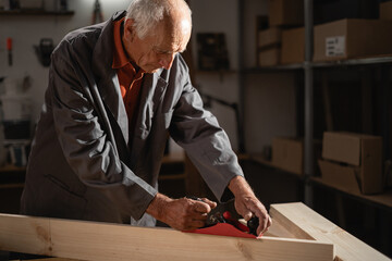 Seventy-year-old carpenter using hand plane to shape wooden items