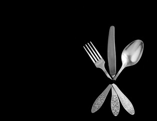 Silver fork, knife and spoon on the black background. Top view. Copy space.