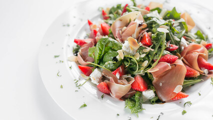Salad with arugula, strawberries, meat, cheese. Seasonal summer salad in a restaurant close-up on a white background