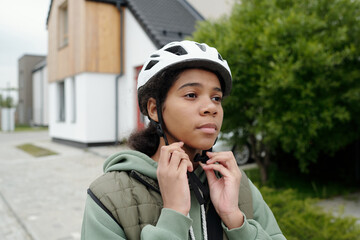 Serene African American postwoman fastening sports helmet while standing in front of camera in...