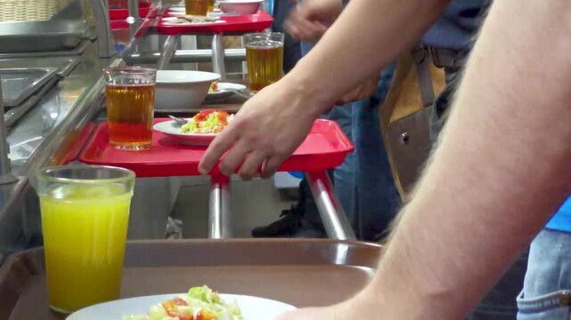 Cafeteria customers choose food and move trays with plates towards the cash register. Fast food concept in a restaurant or cafeteria.