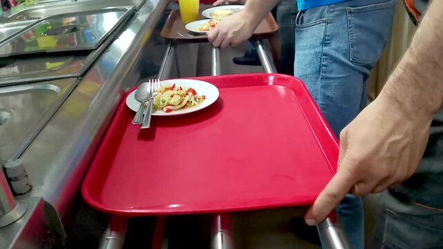 Cafeteria customers choose food and move trays with plates towards the cash register. Fast food concept in a restaurant or cafeteria.