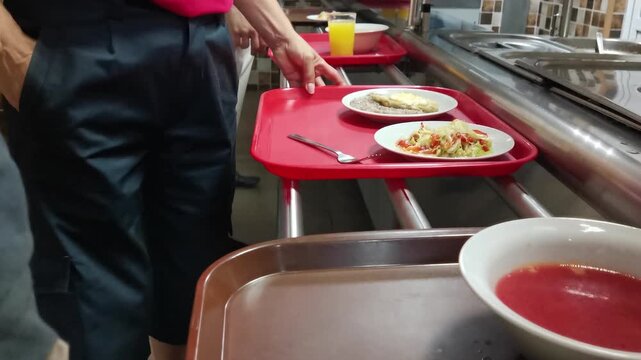 Cafeteria customers choose food and move trays with plates towards the cash register. Fast food concept in a restaurant or cafeteria.