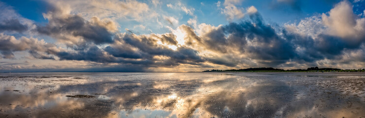 Dramatischer Wolkenhimmel mit tief stehender, verdeckter Sonne über dem gitzernden Watt der Nordseeinsel Föhr bei Ebbe
