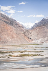Pyanj River flows in Wakhan Valley among rocky high mountains against snow-capped peaks and glaciers in Tajikistan's Tien Shan mountains, landscape for background
