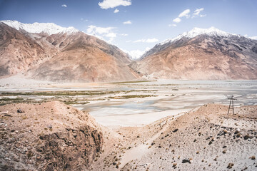 Pyanj River flows in Wakhan Valley among rocky high mountains against snow-capped peaks and glaciers in Tajikistan's Tien Shan mountains, landscape for background