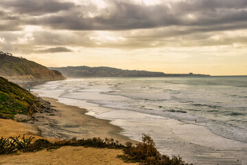 2024-01-10 A VIEW OF THE ROCKY CLIFFS ALONG THE BEACH AT TORREY PINES STATE PARK AND THE PACIFIC OCEAN WITH LA JOLLA IN HTE DISTANCE AND A CLOUDY SKY