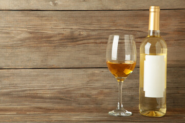 Unlabeled bottled of white wine with half empty wineglass standing on grey wooden background. Space for text