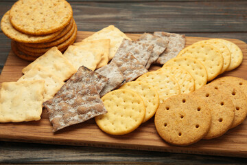 Different crackers on cutting board on black wooden background