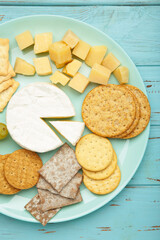 Cheese platter with different cheese and crackers on mint background.