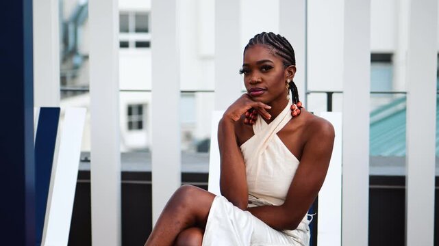 Smiling Black woman with braids, sitting in a lounge chair, in a tight skirt