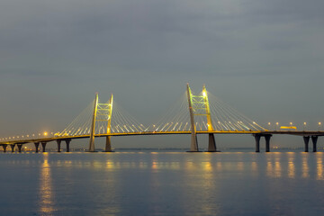 Obraz premium View of illuminated cable-stayed bridge over water surface in evening twilight
